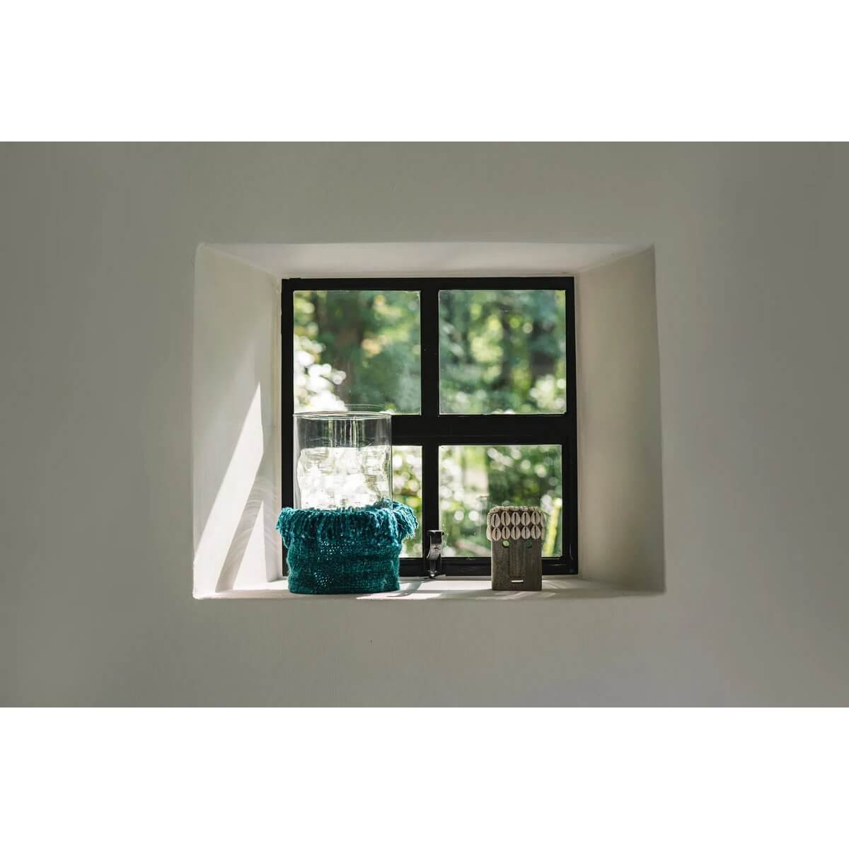 Cozy window nook with light streaming in, featuring a glass vase and a bohemian teal decorative piece, casting shadows on the wall.