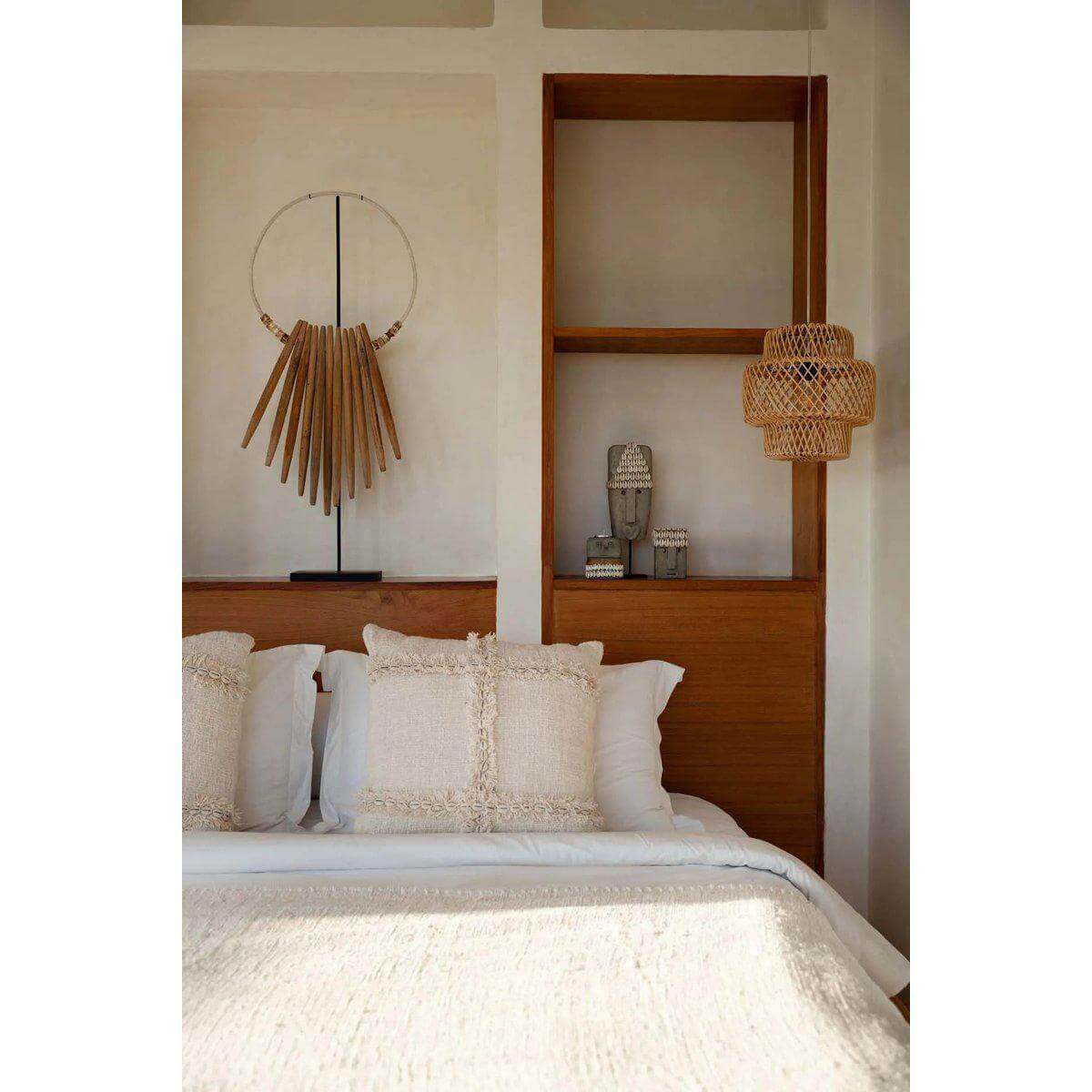 Stijlvolle slaapkamer met Sumba-steenbeeld, houten accenten en geweven lamp voor een rustige ambiance.