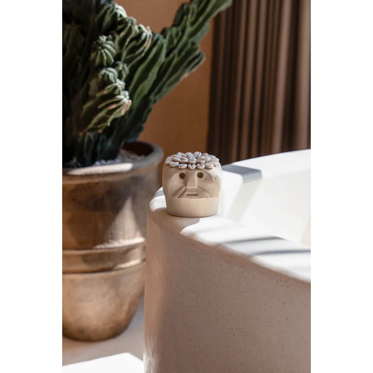 Hand-carved sandstone Sumba statue on a ledge with a cactus in the background, showcasing a Bohemian decor style.
