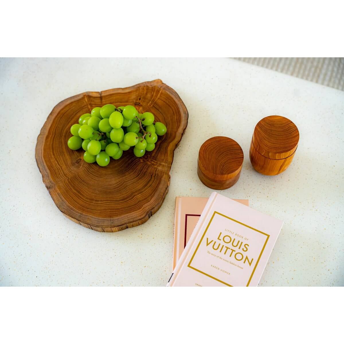 Stylish bohemian setting with green grapes on a rustic wooden tray, wooden containers, and two books on a white table.