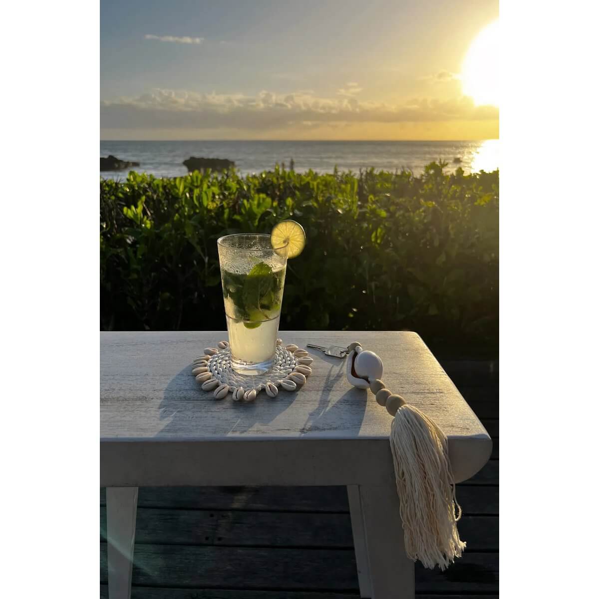Bohemian style scene with Togian keychain and refreshing drink by the sea at sunset, natural white details and ocean vibes.