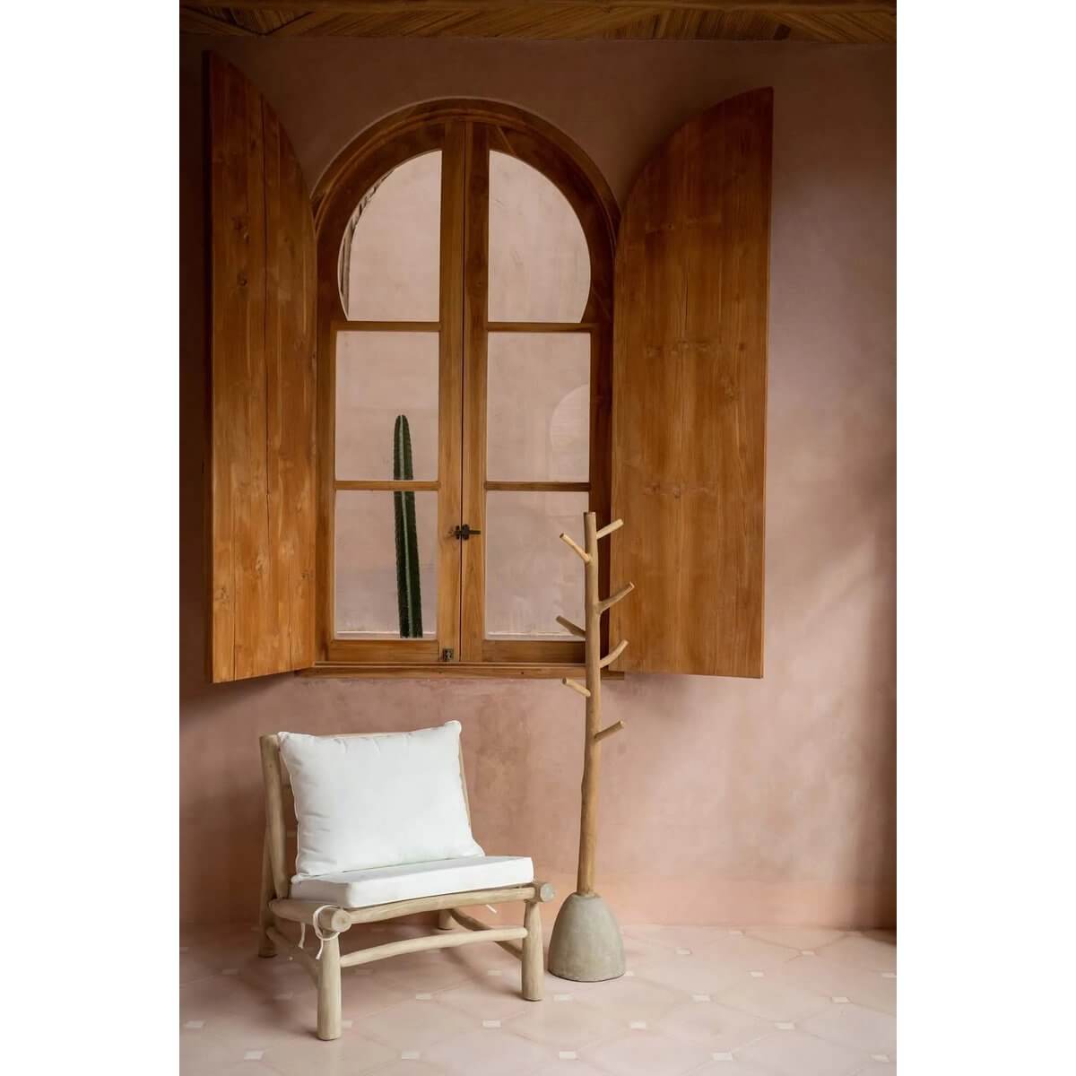 Bohemian style room with beige concrete and teak coat rack, wooden window shutters, and minimalist chair.