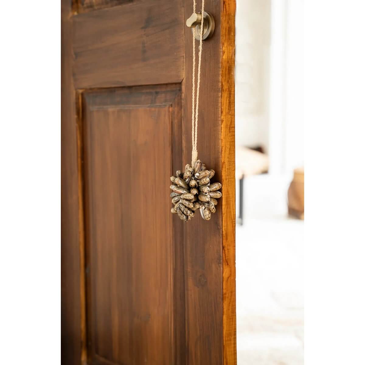 Bohemian brown kauri shell tassel hanging on wooden door, handmade by Balinese artisans for exotic home decor.