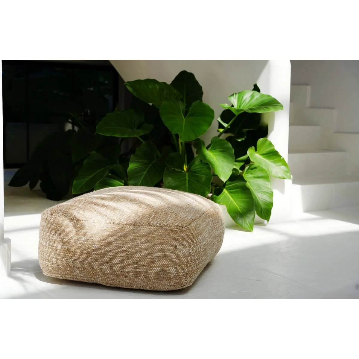 Beige comfortabele poef in een zonnige hoek met planten