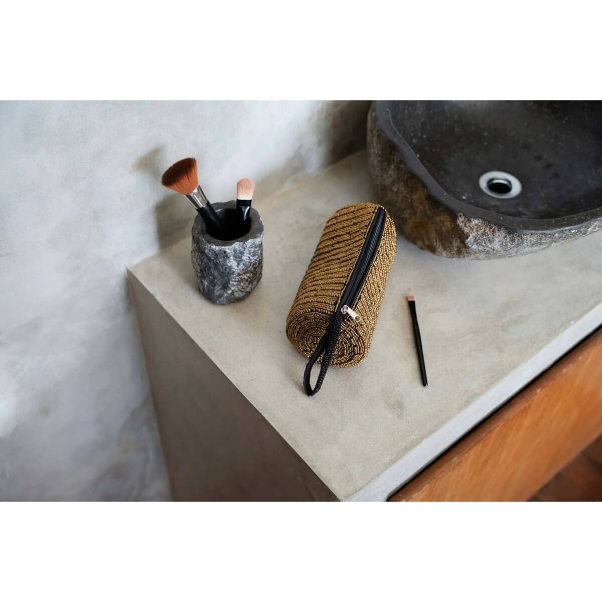 Bohemian-style gold pencil case on bathroom counter, holding brushes and makeup essentials, next to stone organizer.