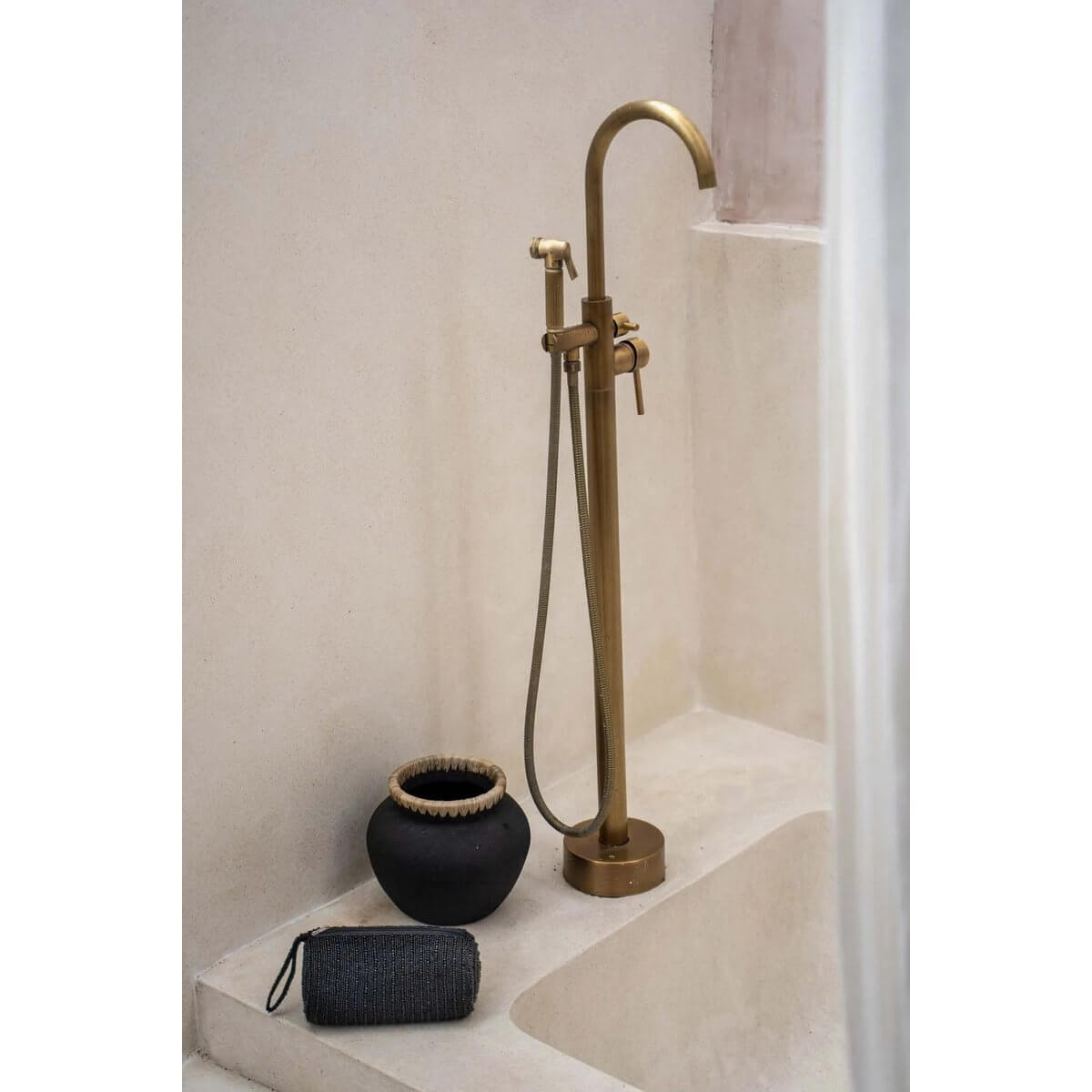 Elegant bathroom with a sleek black Bohemian etui and black vase near a luxurious gold shower fixture on a stone ledge.