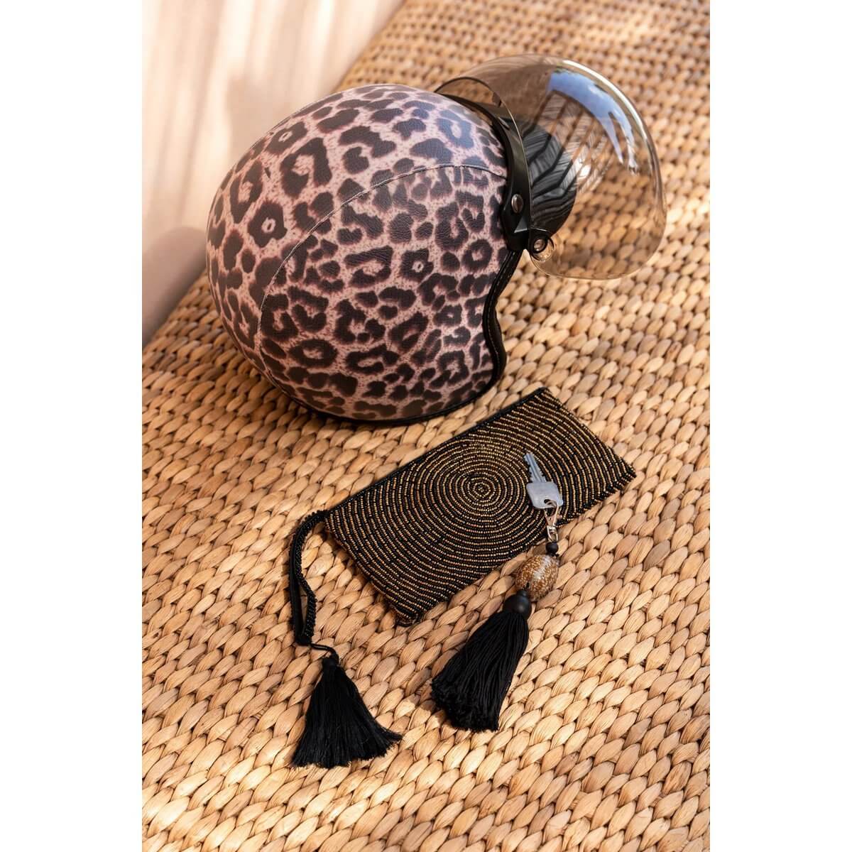 Leopard print helmet with transparent visor paired with a stylish black and gold bohemian clutch on a woven mat.