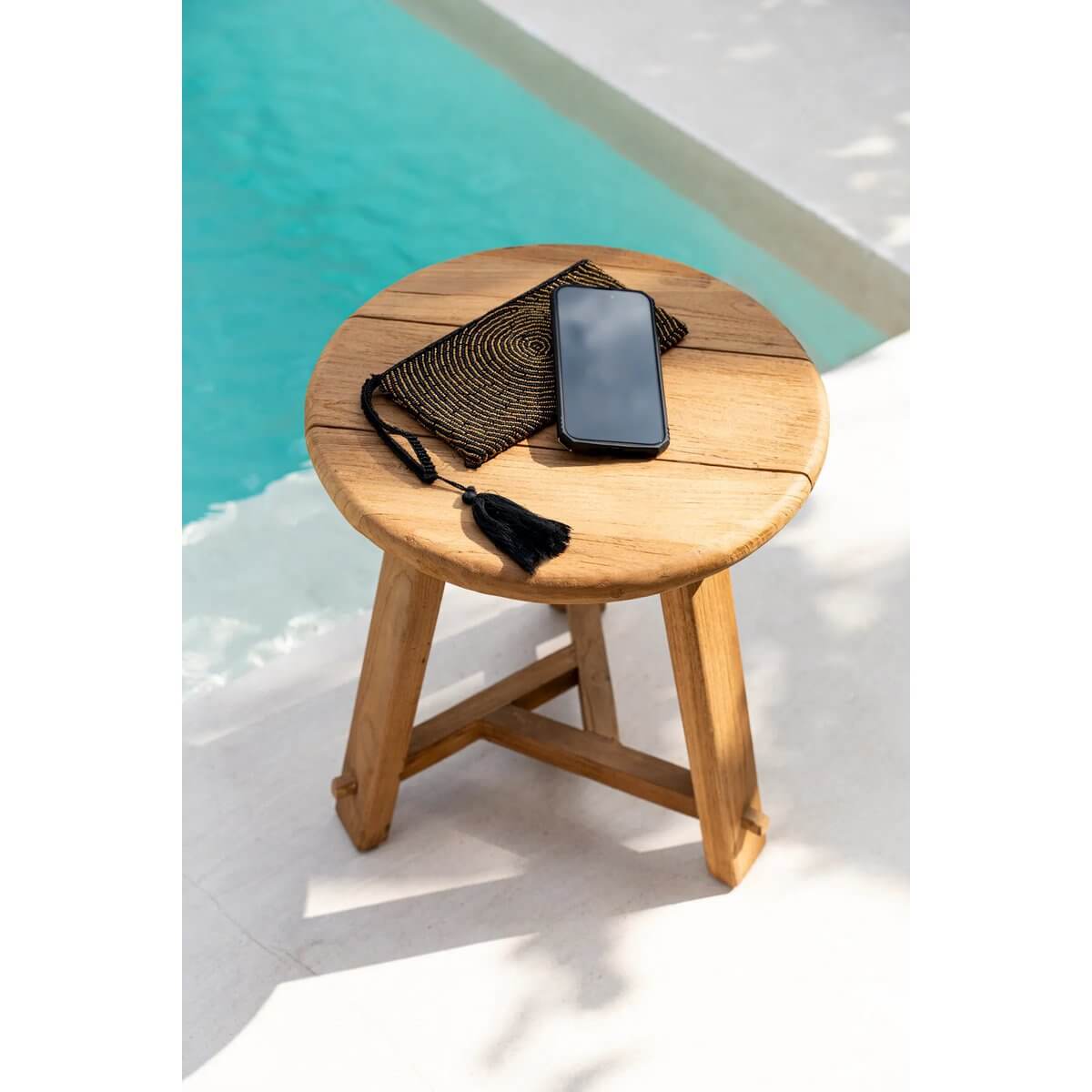 Bohemian style clutch with smartphone on wooden stool by the poolside, evoking a sense of relaxation and chic summer vibes.