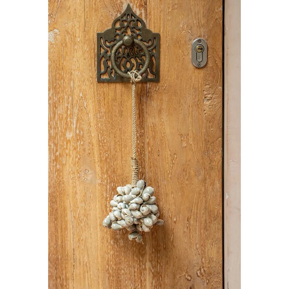 Bohemian shell tassel hanging on a rustic wooden door, adding an exotic touch to home decor.