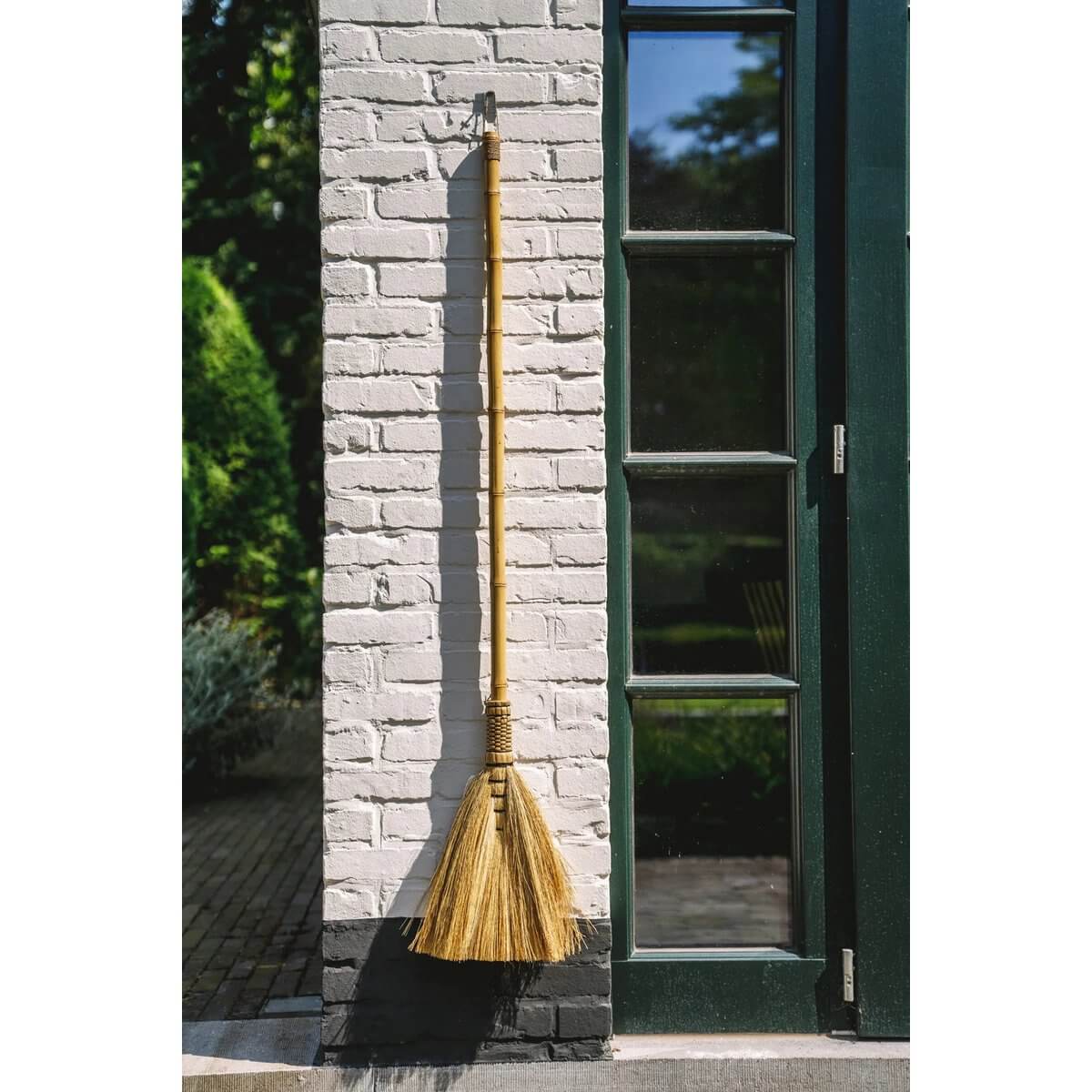 Bohemian-style Indonesian grass broom by Bazar Bizar Living against a white brick wall, ideal for decorative interior use.