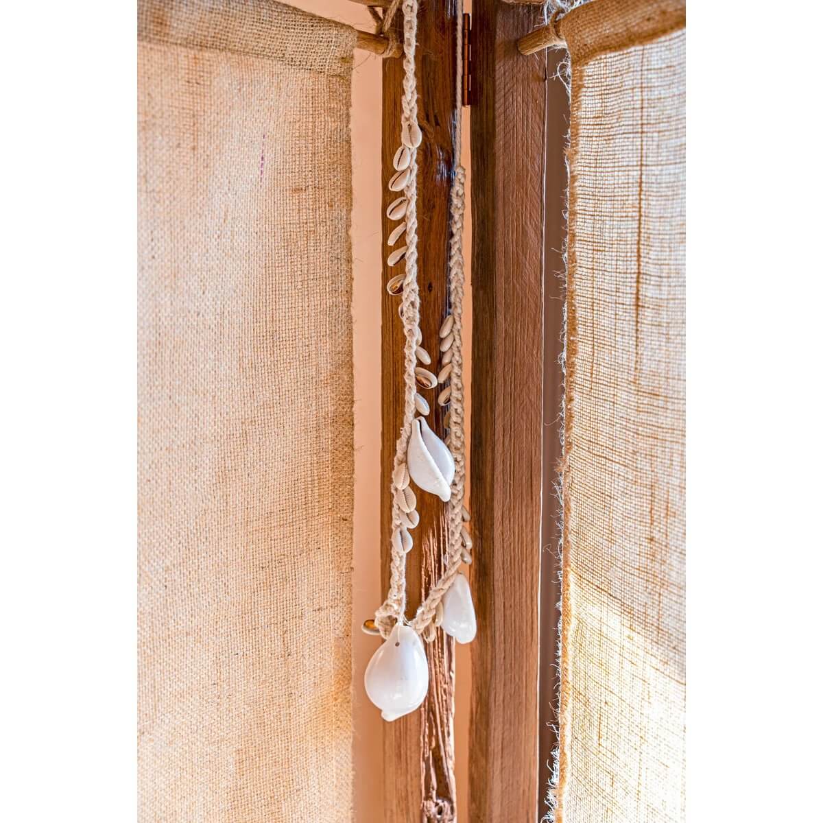 De grote witte kauri schelp ketting hangt langs een rustieke houten deur, straalt kustflair en bohemien charme uit in huisdecor.