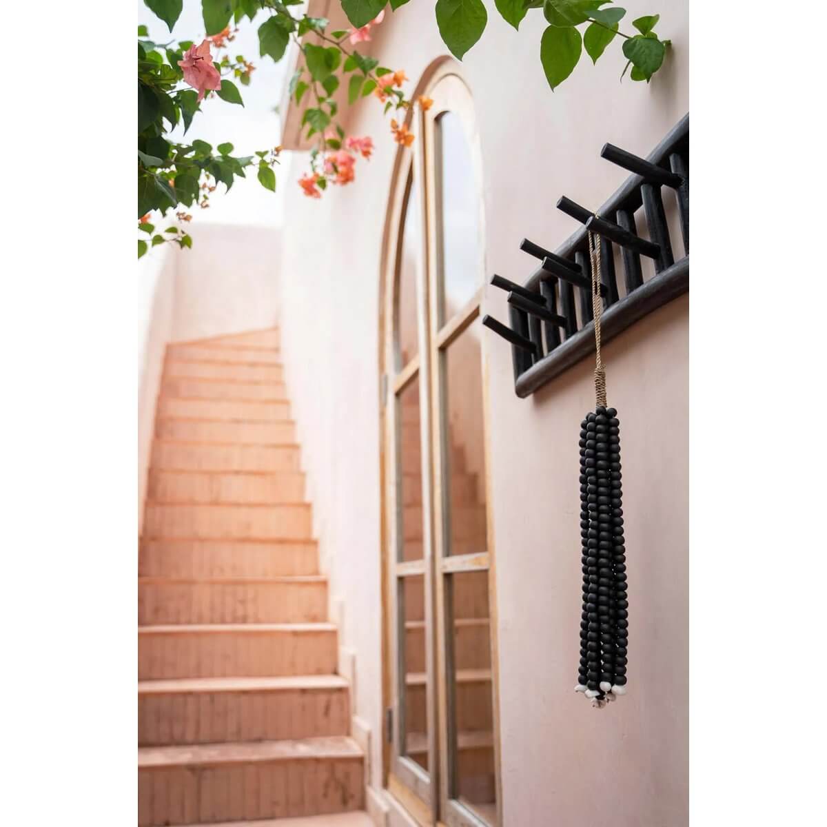 Handmade black wooden bead tassel hanging on a rustic hook, exuding a bohemian charm on a stylish terrace with lush greenery.