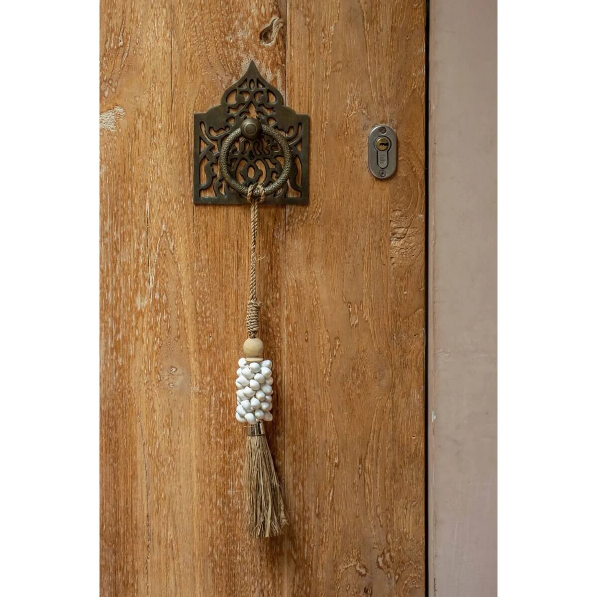 Bohemian kauri and raffia tassel hanging on a rustic wooden door, adding an exotic touch to home decor. Crafted by Balinese artisans.