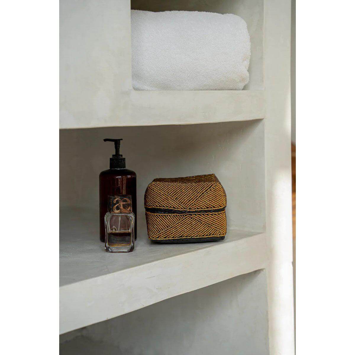 Handgemaakte Balinese kralendoos goud op plank bij verzorgingsproducten, ideaal voor decoratie of opslag, geïnspireerd door rituele ceremonies.