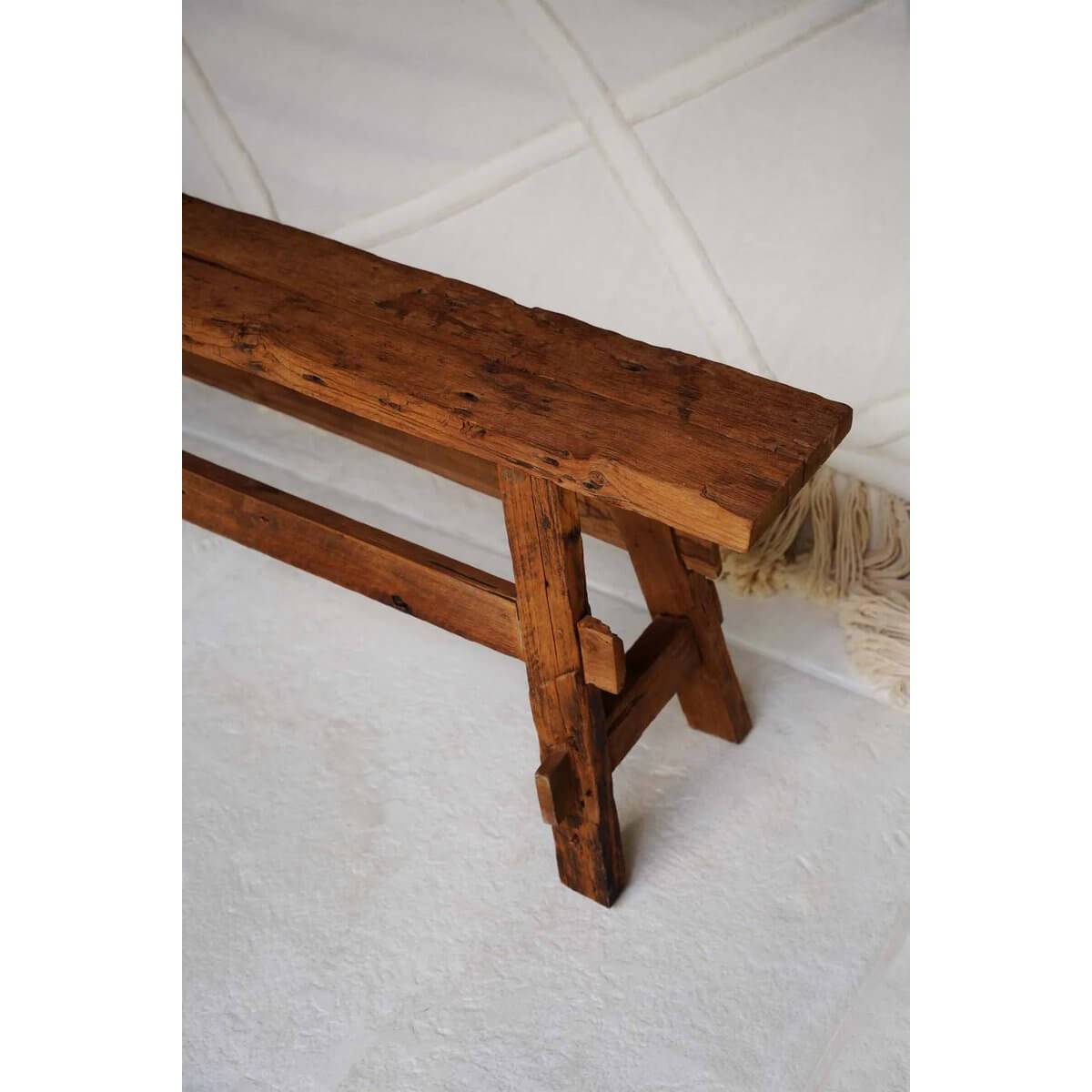 Bohemian wooden bench with rustic teak finish, showcasing natural beauty and simple lines on a textured white background.
