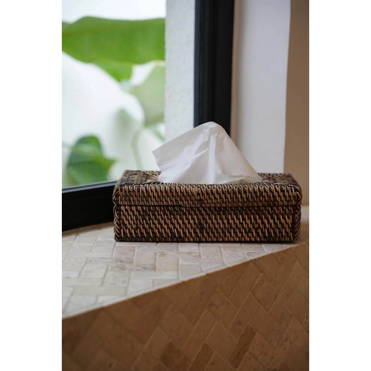 Rattan Classic Tissue Box in natural brown, adding elegance and style to any room, placed on a windowsill with greenery outside.