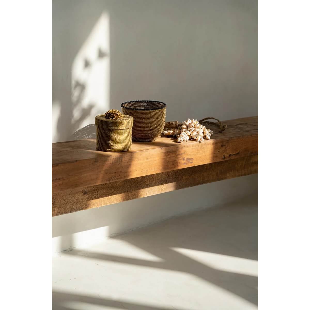 Rustic wooden table with woven baskets and a handmade shell tassel, adding a bohemian touch to home decor.