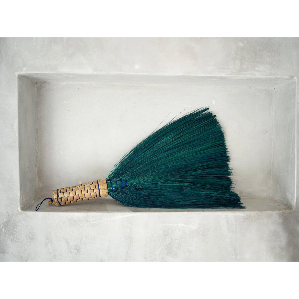 Turquoise Indonesian hand broom on display, perfect for a Bohemian interior, made from grass for sweeping dust and dirt stylishly.