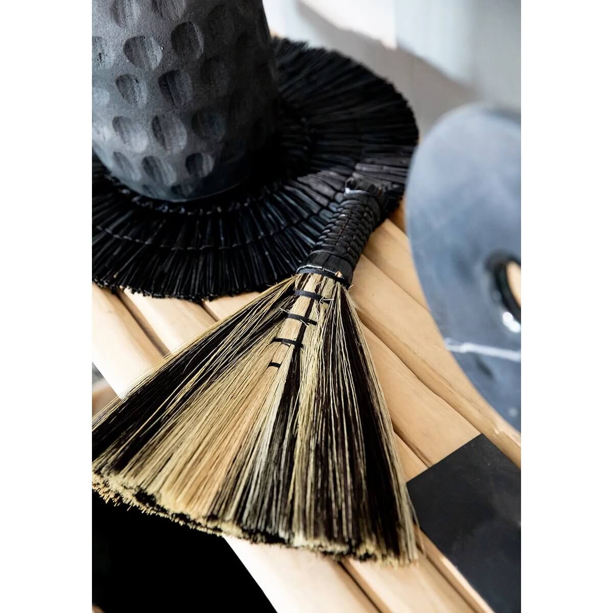Bohemian black natural Indonesian hand-broom made from grass, stylishly displayed as a decorative piece in a modern setting.