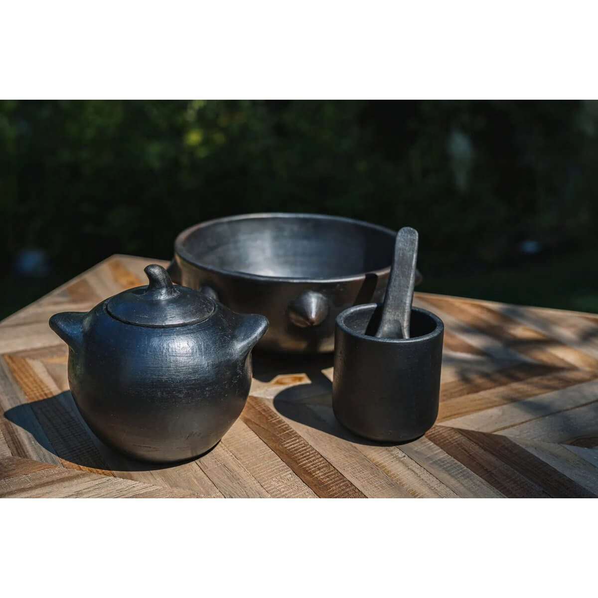 Bohemian black-burnt ceramic set, including a lidded jar, small bowl, and spoon, perfect for serving sauces and tapas on a wooden table.