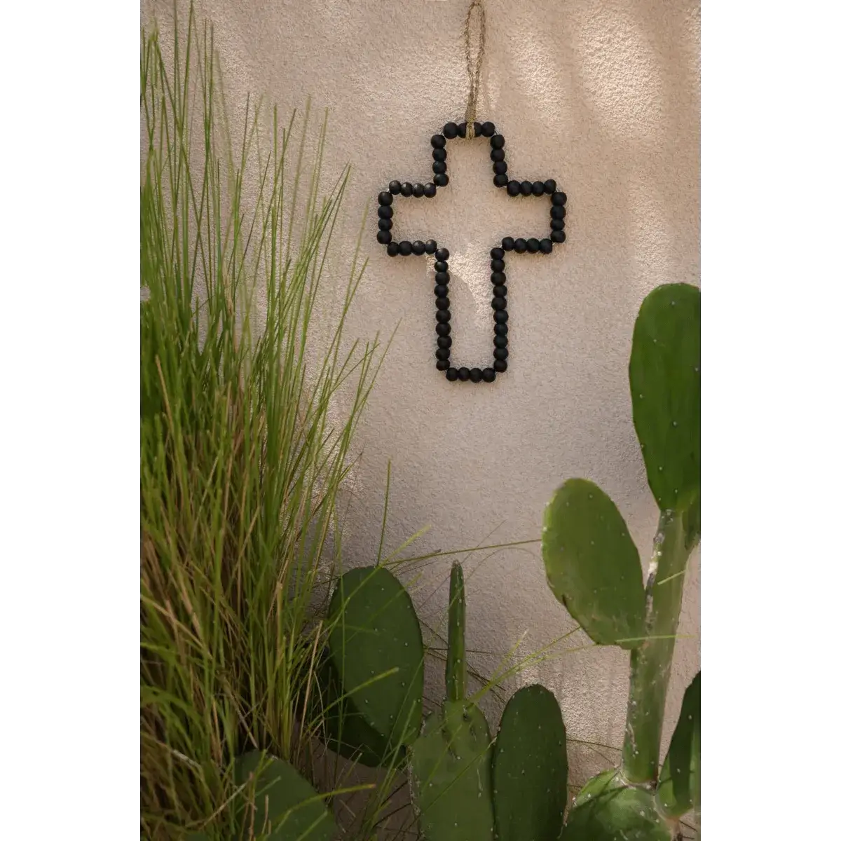 Bohemian style wooden cross wall decor with black beads, surrounded by plants, handcrafted by Bazar Bizar Living. Perfect for home decor.