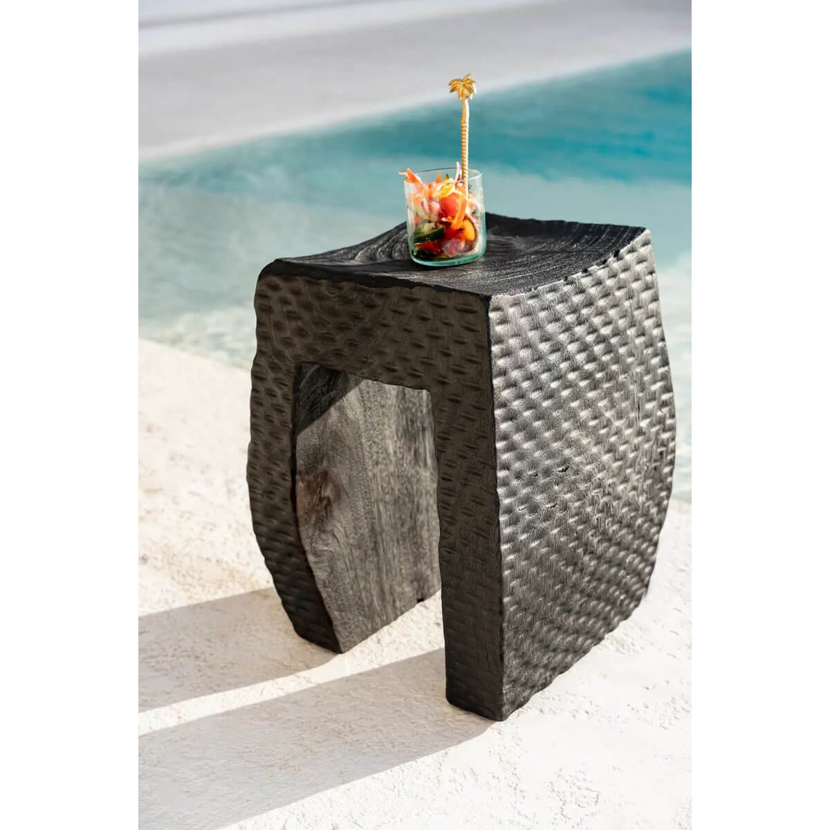 Bohemian style On the Rocks glass with colorful drink, placed on a textured outdoor table with a poolside view.