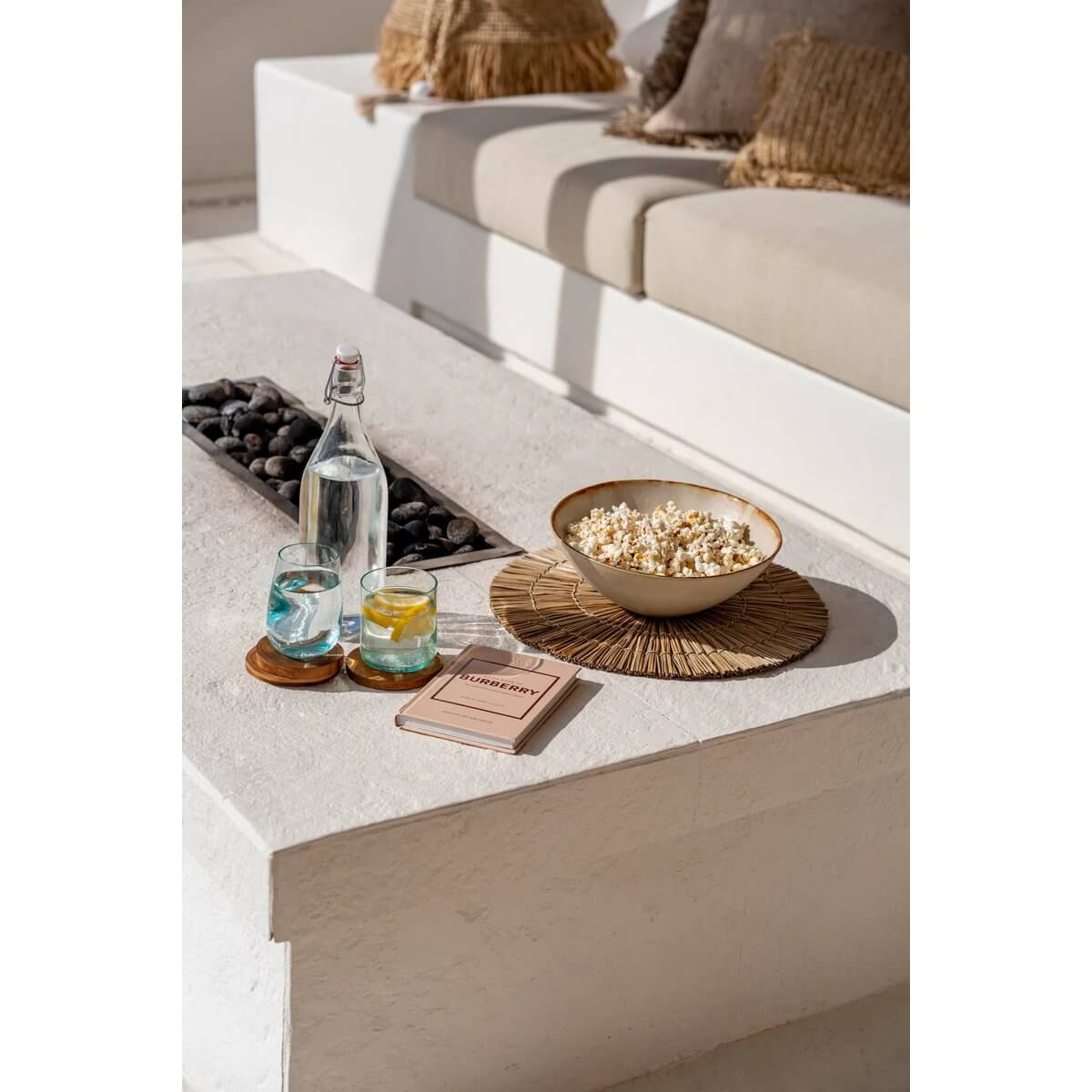 Bohemian style setup with On the Rocks recycled glass, popcorn and book on an outdoor white table, exuding relaxation and eco-friendliness.