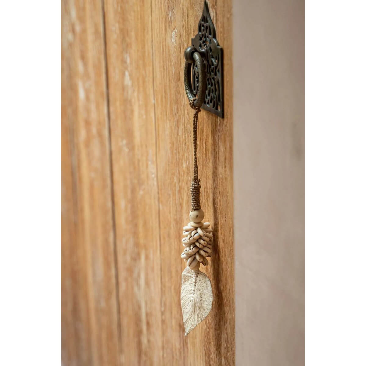Handmade shell tassel by Bazar Bizar, hanging on a wooden door, adding a bohemian touch to home decor.