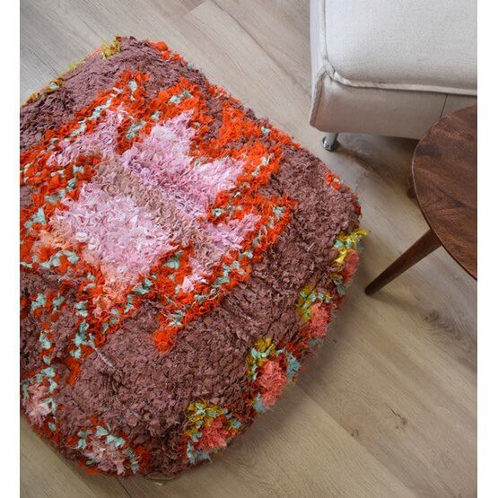 Kleurrijk Marokkaans Boucharouite vloerkussen in woonkamer, handgemaakt van gerecycled textiel, benadrukt traditionele weeftechniek.