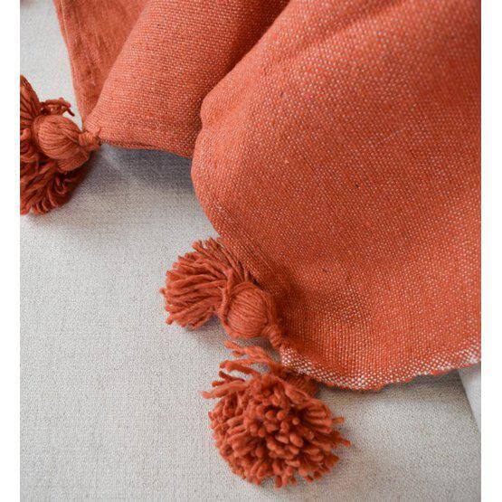 Oranje Marokkaanse pompondeken op bed, ideaal voor een gezellig interieur en geschikt voor moderne en bohemien stijlen.