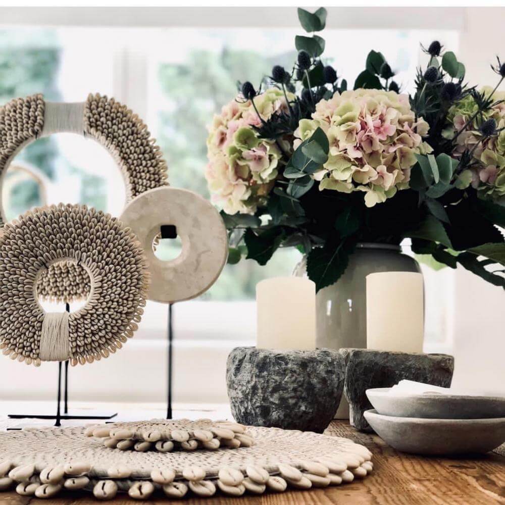 Schelpenketting op standaard en bloemen in vaas, perfecte combinatie voor een Ibiza woonkamer sfeer vol kustgevoel en ontspanning.