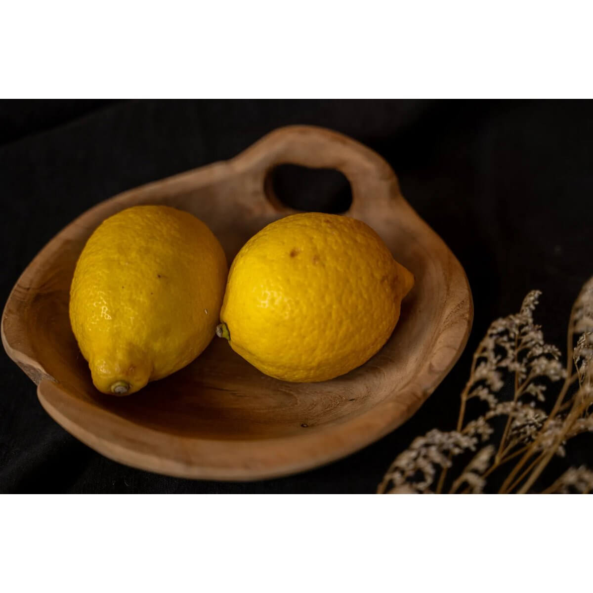 Rustic teakhouten schaal met handvat, bohemian charm met citroenen en bloemen op een donkere achtergrond