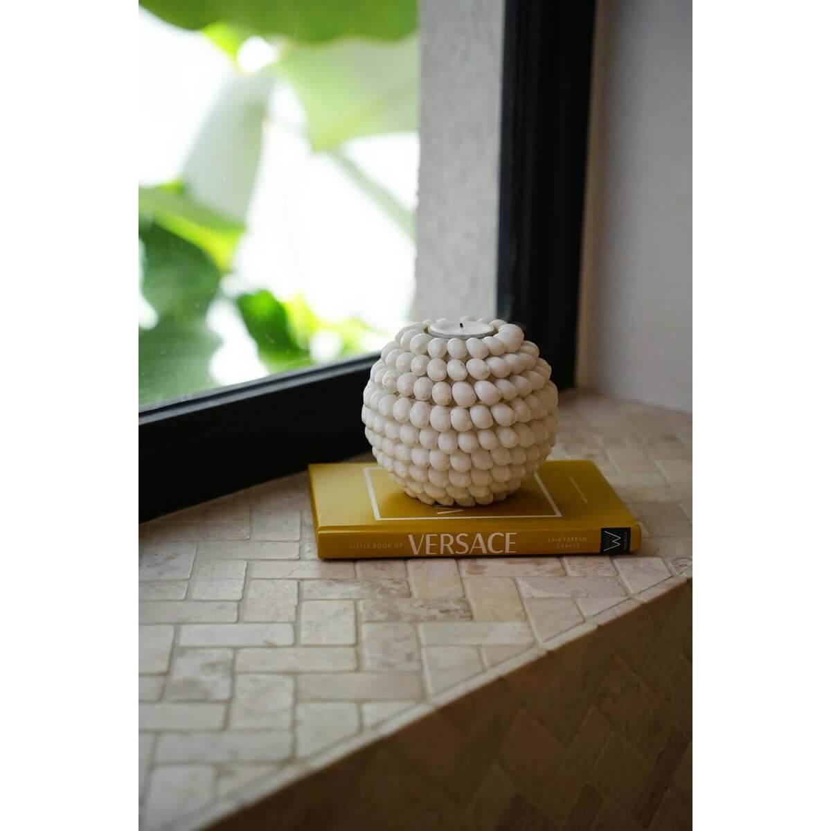 Bohemian Bubble Candle Holder with white shell design on a yellow book by a window, creating a cozy ambiance.