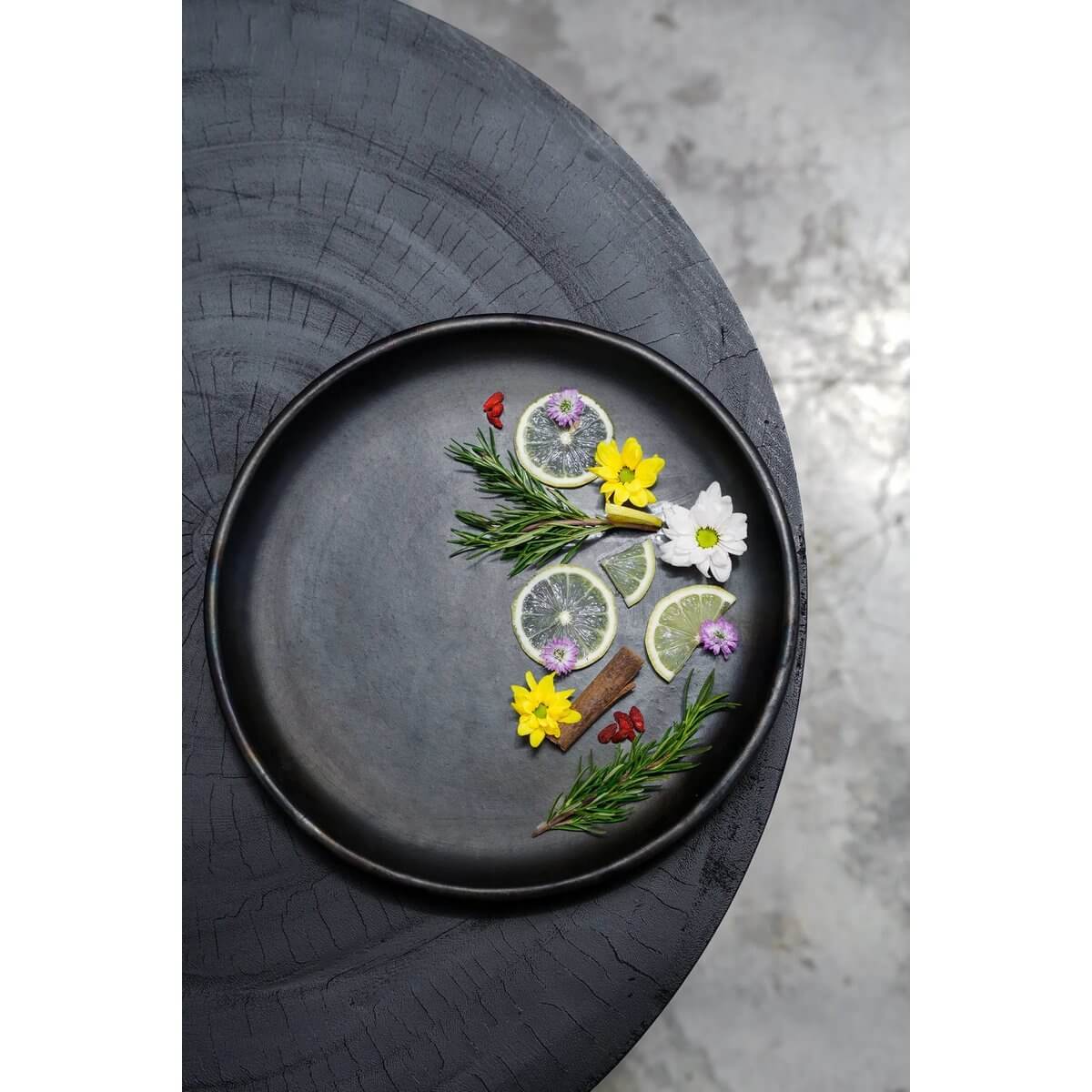 Bohemian style black terracotta plate with floral garnish on textured table, perfect for elegant dining by Bazar Bizar Living.