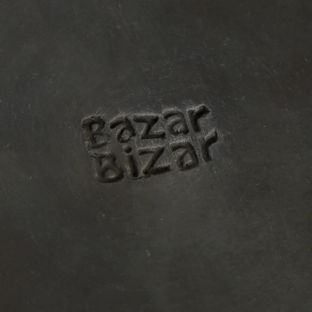 Close-up of Bazar Bizar logo embossed on a dark ceramic surface.