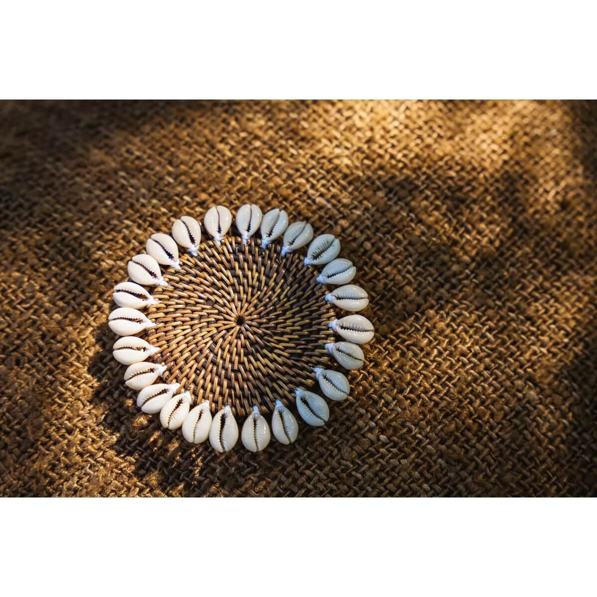 Bohemian Colonial Shell Coaster with woven design and shell border on natural brown surface, adding tropical island style to your home.