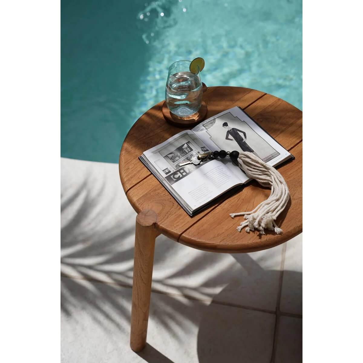 Bohemian Cotton Wood Keychain on wooden table by pool, featuring natural tassels and black beads, next to glass of water and open book.