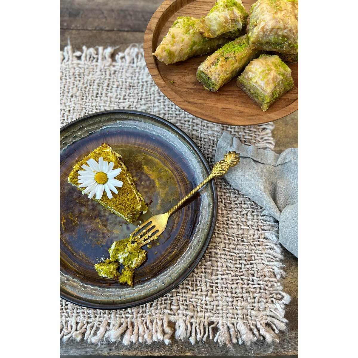 Gezellig dessert gepresenteerd op katoenen wafelstructuur placemat met groen baklava en bloemenversiering.
