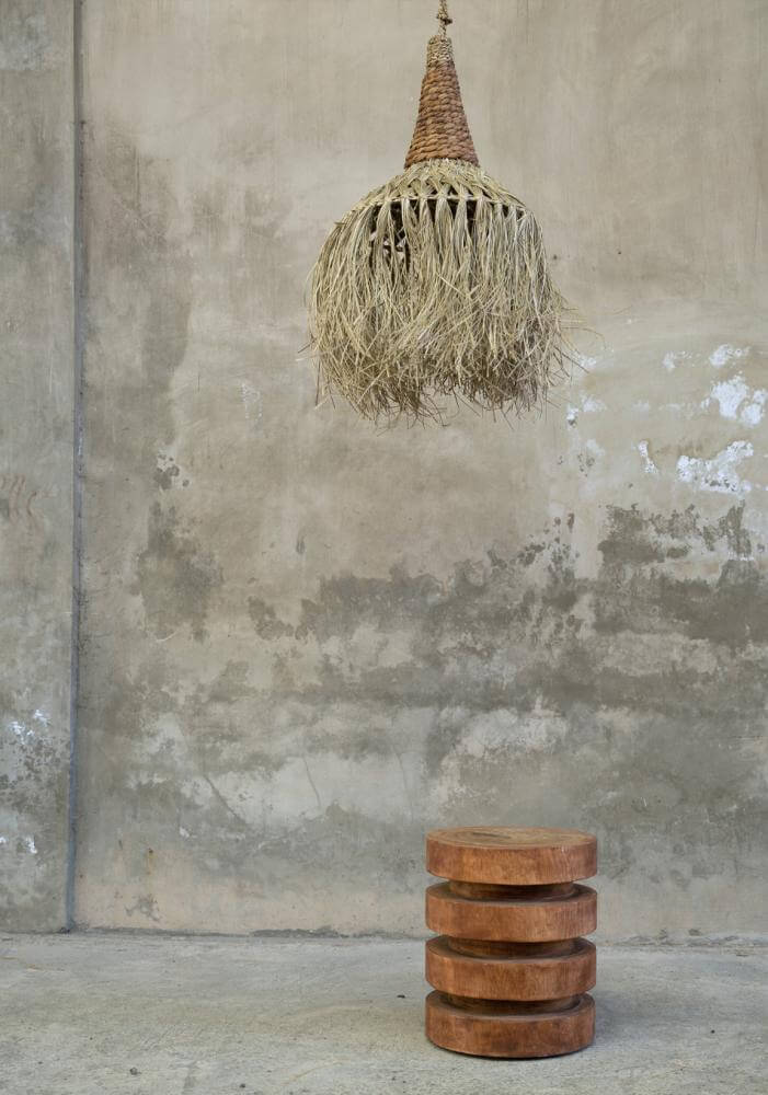 Een natuurlijke hanglamp van sisal en bananenblad, strand geïnspireerd, hangt boven robuuste houten krukjes op een ruwe achtergrond.