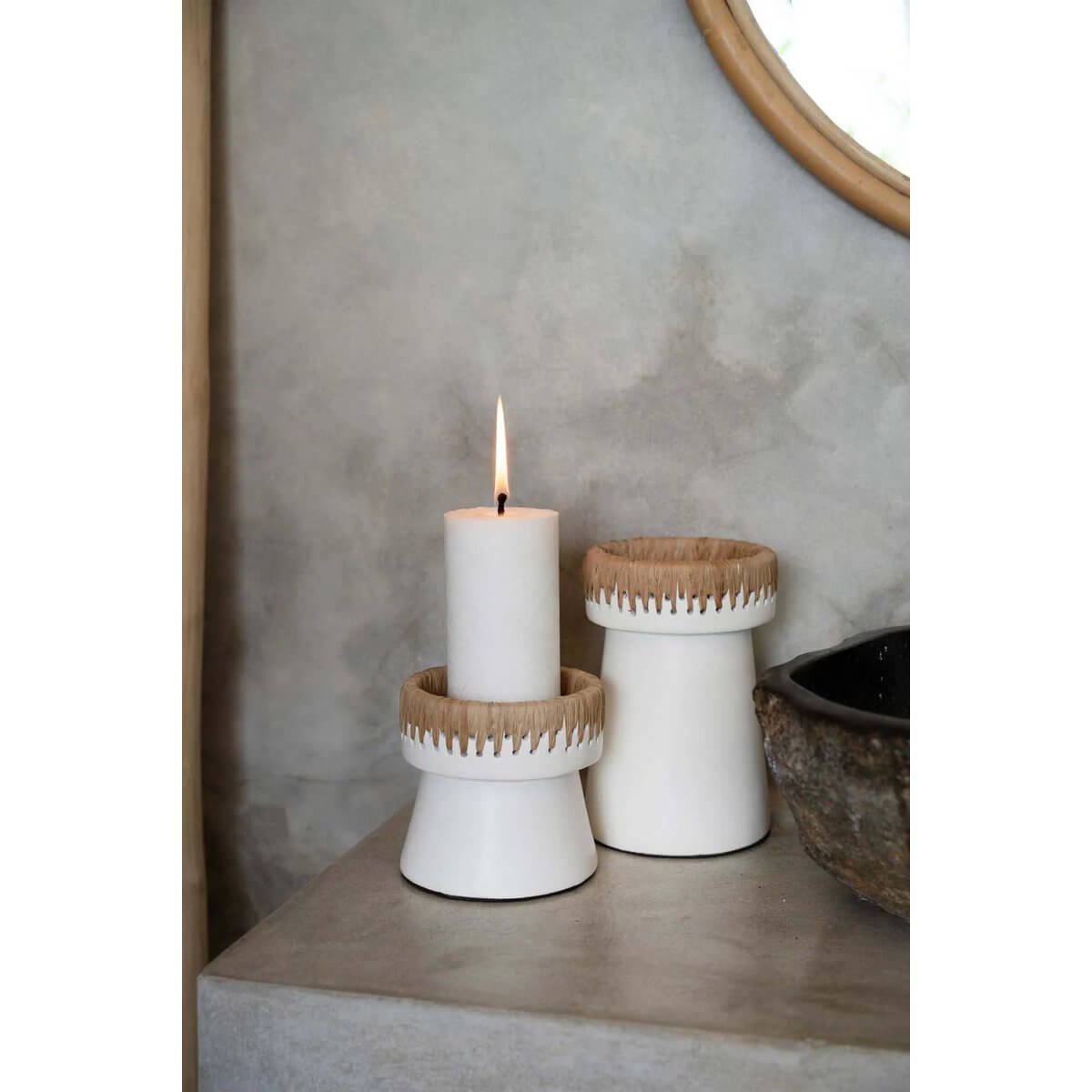 White terracotta candle holders with raffia accents, creating a bohemian look on a table. Stylish addition for home decor.