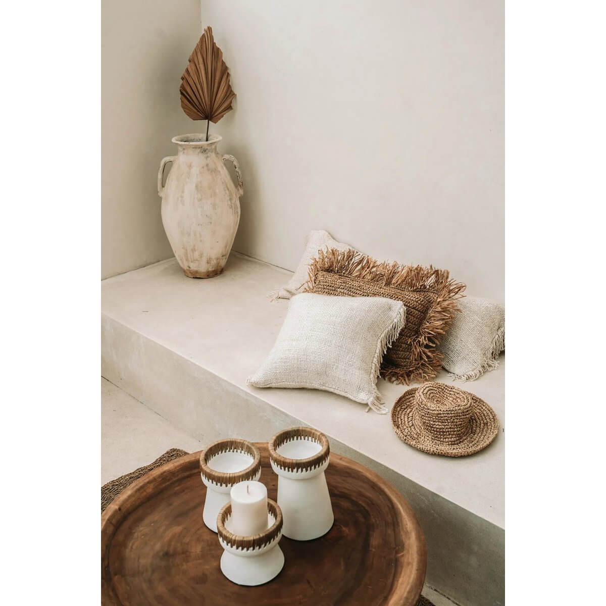 Bohemian style setting with white terracotta candle holders and raffia accents on a rustic wooden table.