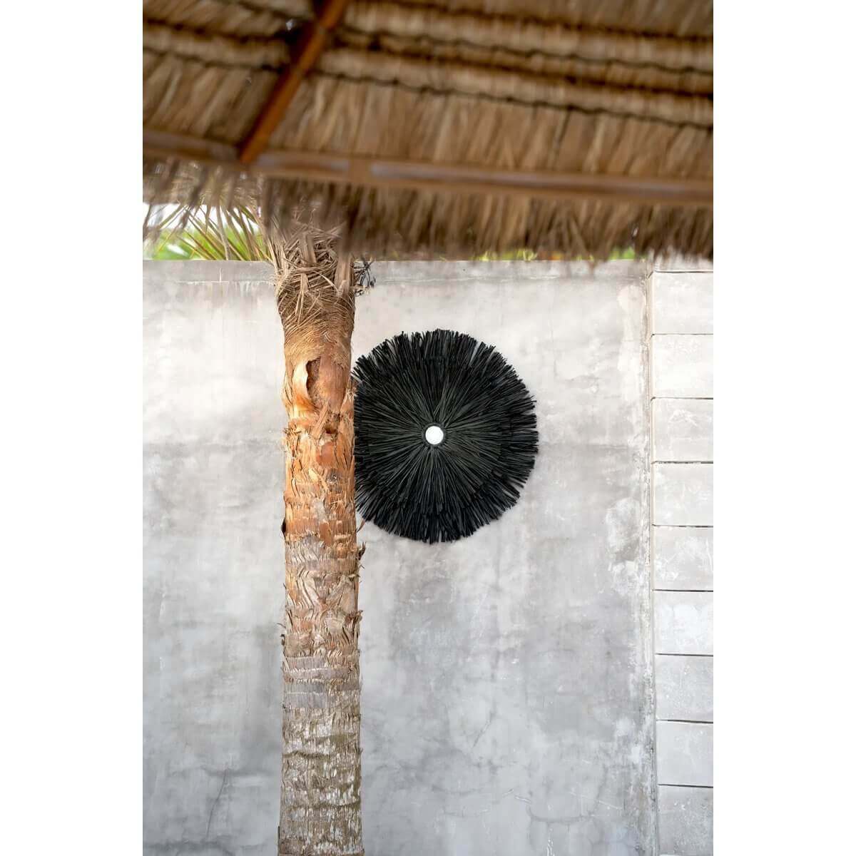 Raffia Juju muurdecoratie in zwart op betonmuur naast palm - perfect voor een bohemien interieur en tuin, door Bazar Bizar Living.