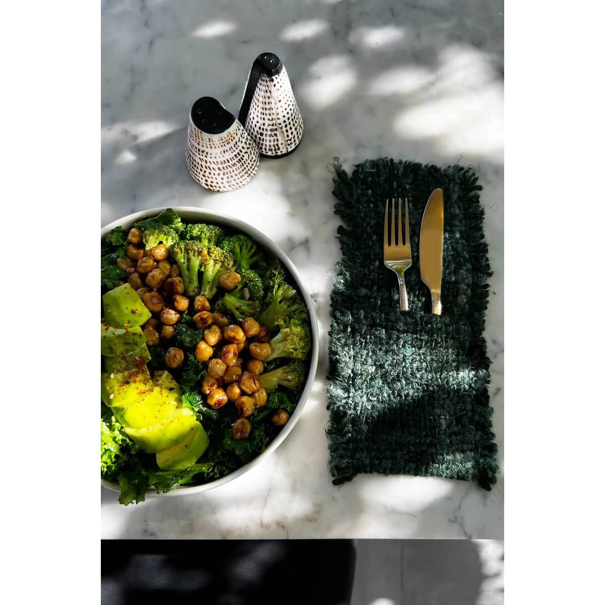 Bohemian Salt and Peppa Shell Set on a marble table with salad and cutlery.