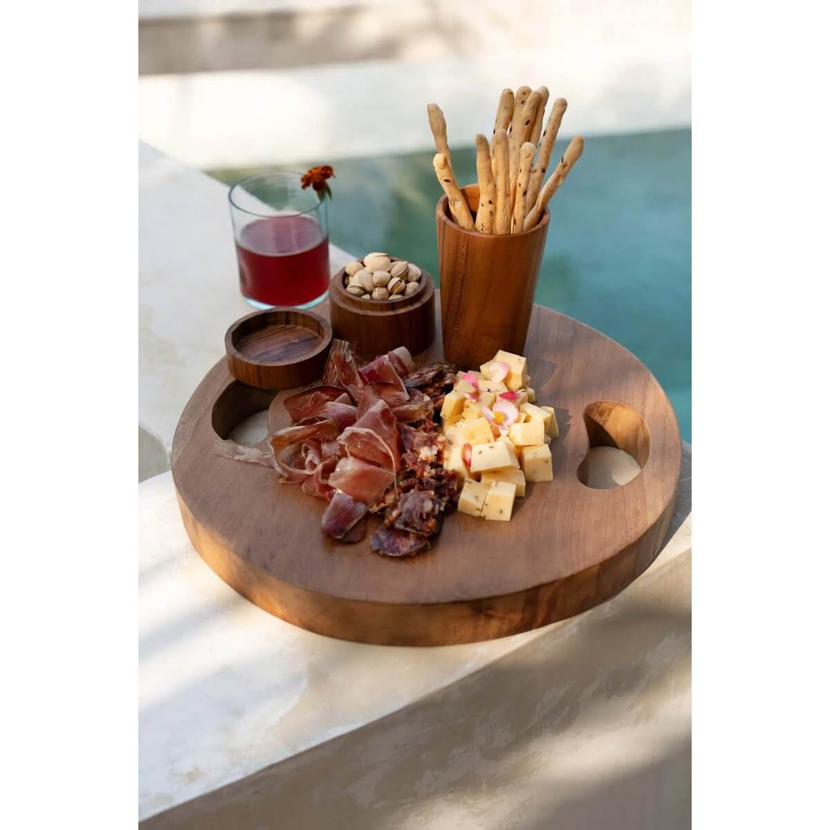 Bohemian-style teak root cup and cheese platter by the pool, featuring cured meats, cheese, breadsticks, and pistachios.