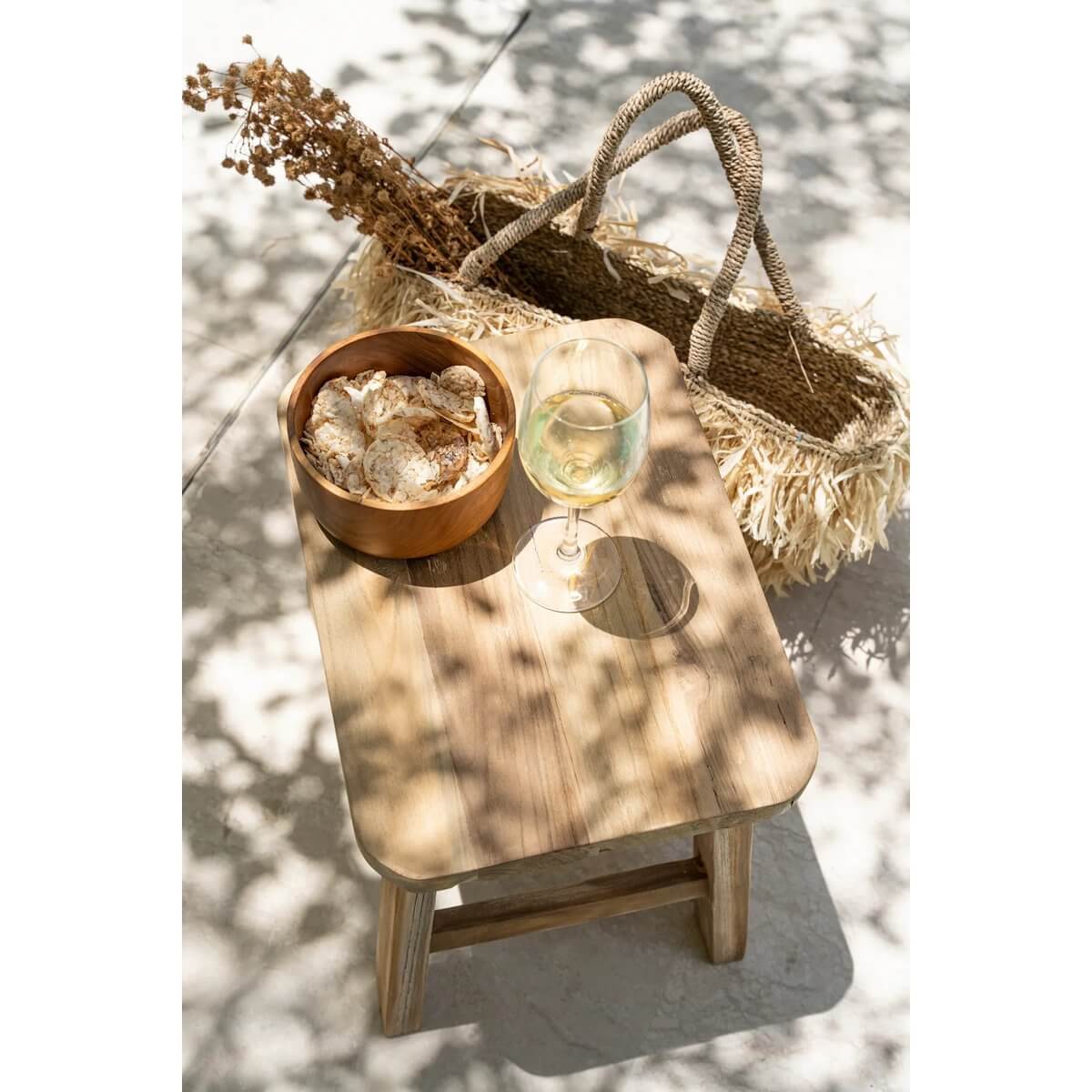 Bohemian style outdoor setup with a teak salad bowl on a wooden table, accompanied by a wicker basket and glass of wine.