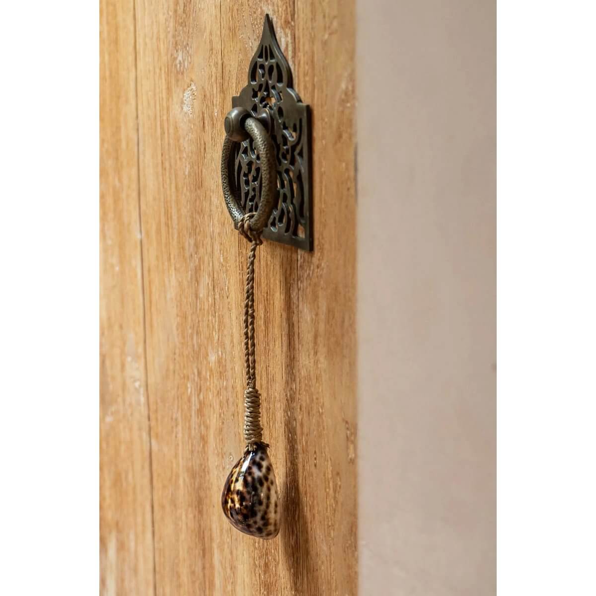 Tranquility Tassel with tiger shell hanging on a wooden door, adding a bohemian touch by Bazar Bizar Living.