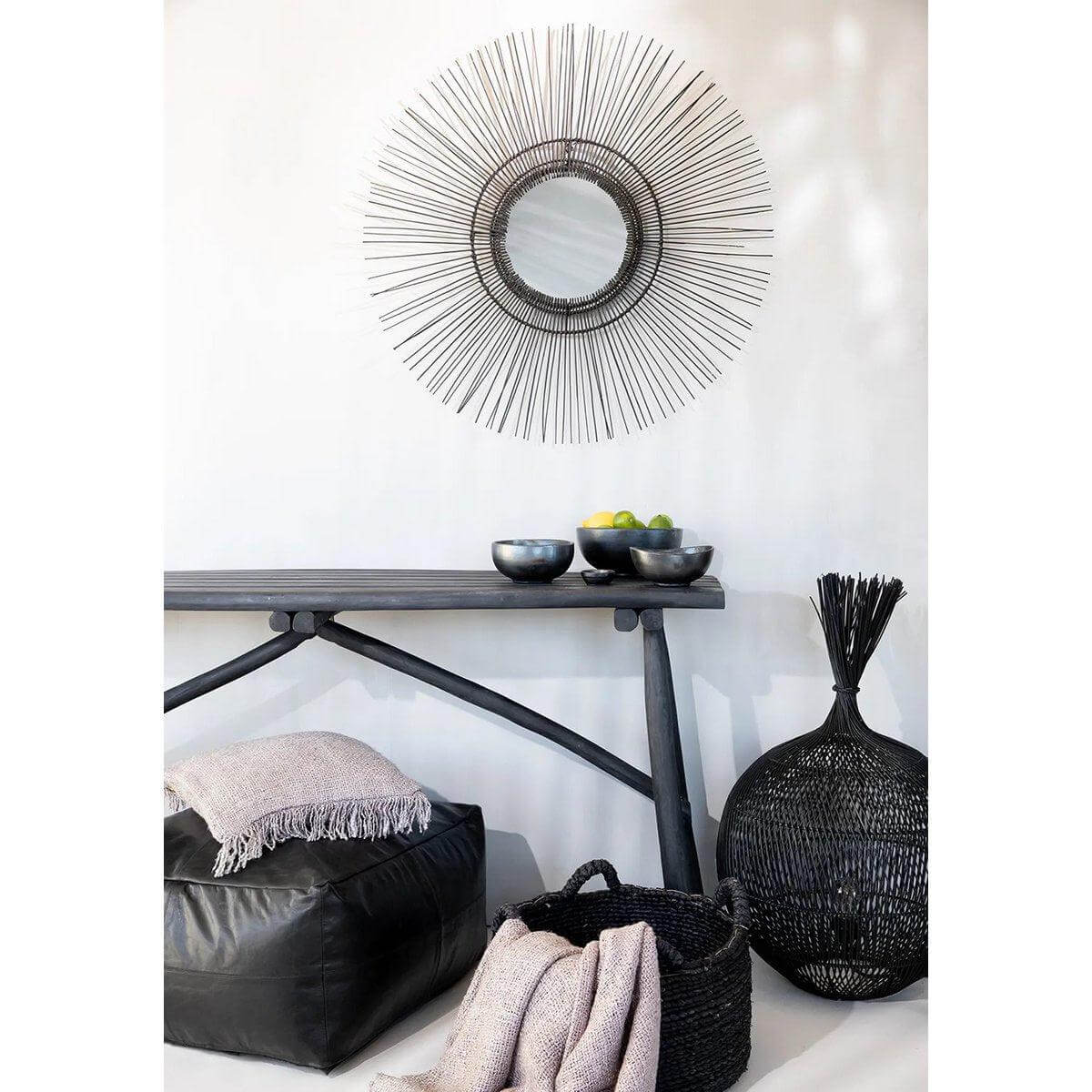 Zwarte tropische spiegel in jaren 70-stijl boven een moderne interieurtafel, met decoratieve manden en kussens.