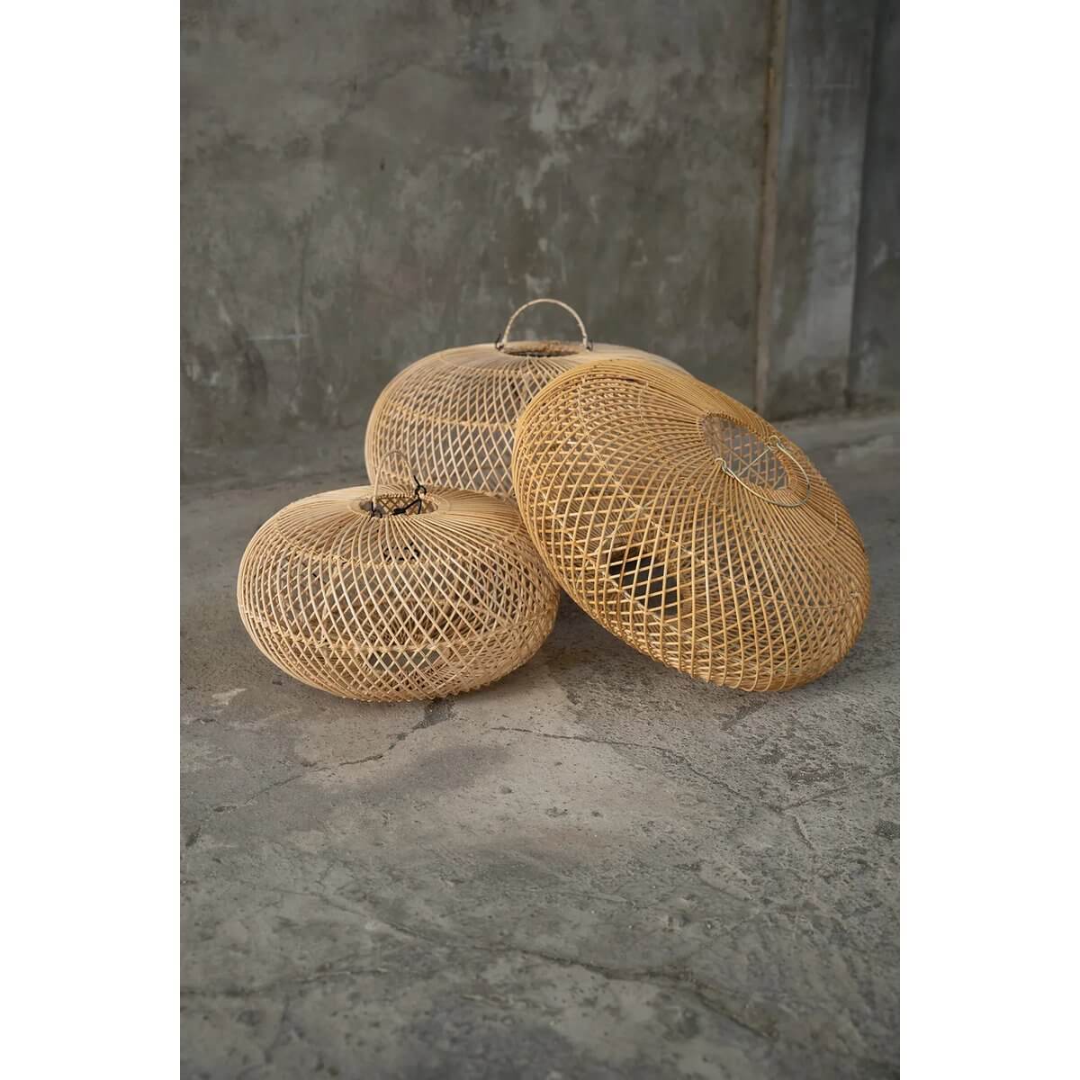 Drie rotan hanglampenkappen van Wholly Hanger in natuurlijke tinten op ruwe betonnen ondergrond.