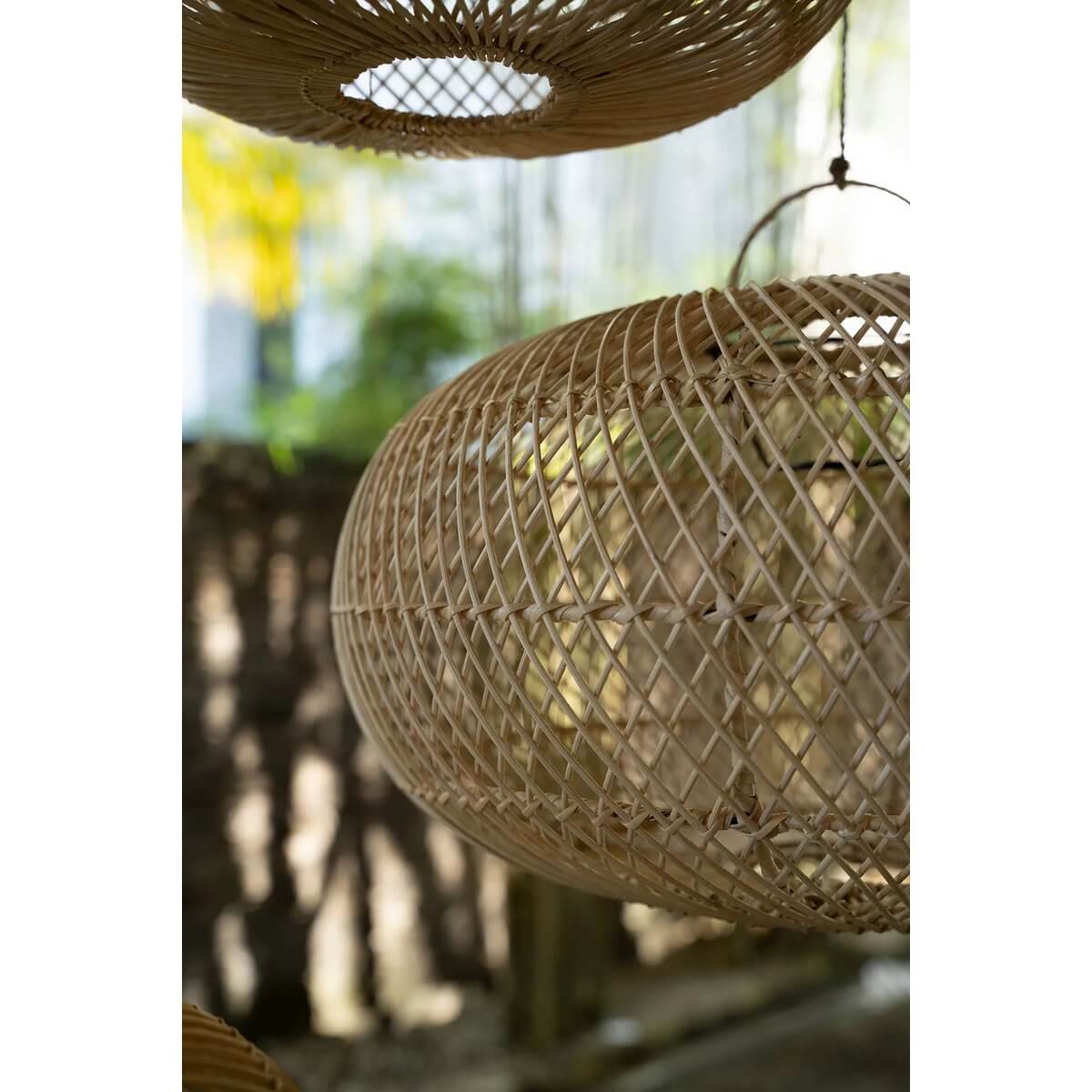Rotan hanglamp De Wholly in een zonnige tuin, schaduwen spelend op het interieur. Perfect voor sfeervolle verlichting.