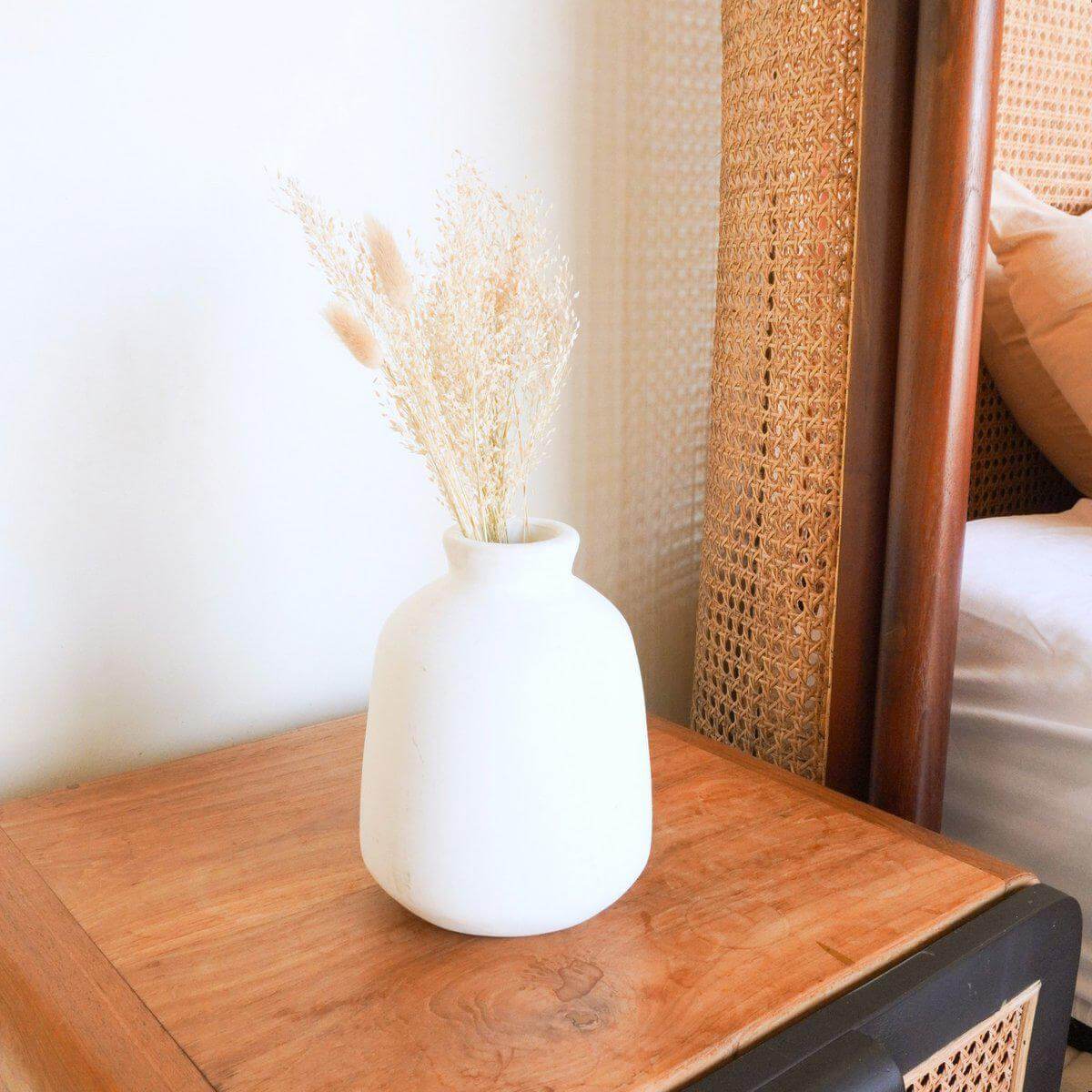Alt Tag: Handgemaakte Bawa-vaas van witte klei, ideaal voor boho bloemen, op een houten tafel met gedroogde graspluimen.